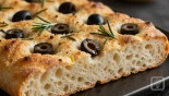 Een stuk focaccia met olijven en rozemarijn.