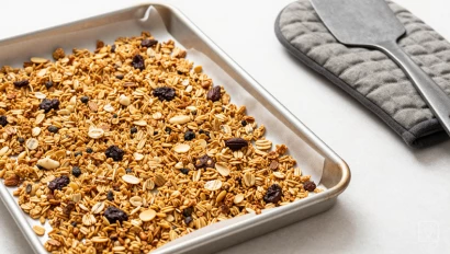 Gebakken granola op een bakplaat met een spatel en ovenwanten.