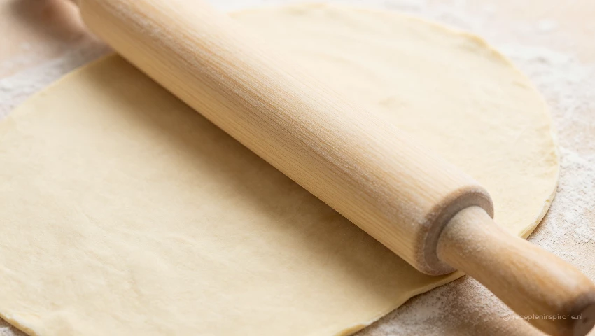 Close-up van een deegrol die over deeg gaat.